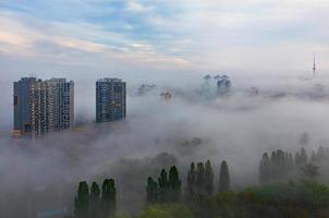 een dikke mist daalde in de vroege ochtend neer op de slapende stad en strekt zich uit tussen residentiële hoogbouw en over het groene park. foto