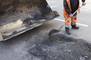 gedeeltelijke reparatie van de asfaltweg. de werknemer maakt een slecht deel van de weg schoon foto