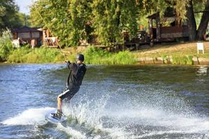 een wakeboarder raast met hoge snelheid door het water langs de groene oever van de rivier. foto