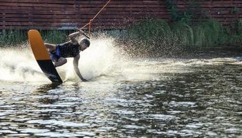 een wakeboarder raast met hoge snelheid door het water en tilt in een scherpe bocht een waterkolom op.