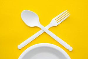 plastic witte gekruiste vork, lepel en bord op gele achtergrond