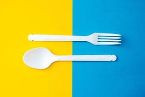 plastic witte lepel en vork op gele en blauwe achtergrond