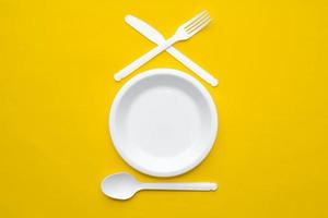 plastic witte vork, mes, lepel en bord op gele achtergrond foto