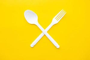 plastic witte gekruiste vork en lepel op op gele achtergrond foto