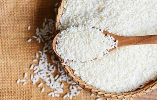 jasmijn witte rijst op houten lepel op de mand in de zak, oogst rijst en voedselkorrels kookconcept