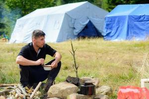 een man kookt tijdens het reizen in de natuur op de achtergrond van tenten foto