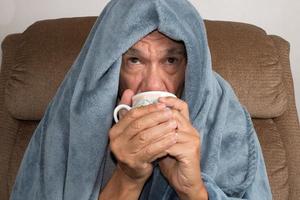volwassen man voelt zich niet goed wikkel in een deken die thee drinkt foto