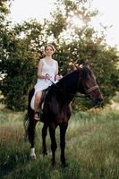 meisje in een witte zomerjurk op een wandeling met bruine paarden foto
