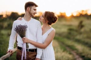 meisje in een witte zomerjurk en een man in een wit overhemd op een wandeling bij zonsondergang met een boeket foto