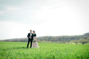 de bruidegom in een bruin pak en de bruid in een ivoorkleurige jurk op een groen veld foto