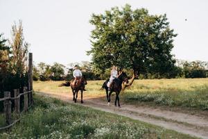 meisje in een witte zomerjurk en een man in een wit overhemd op een wandeling met bruine paarden foto