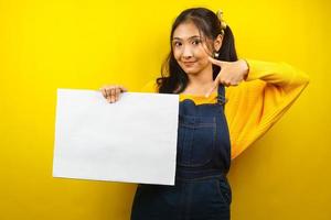 mooie en schattige jonge vrouw vrolijk met lege lege banner, plakkaat, wit bord, leeg bord, wit reclamebord, iets presenteren in kopieerruimte, promotie foto