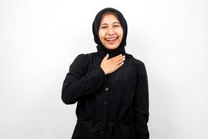 Mooie en vrolijke jonge Aziatische moslimvrouw met handen die borst houden die op witte achtergrond wordt geïsoleerd foto