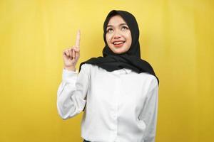 mooie jonge aziatische moslimvrouw glimlachend zelfverzekerd, enthousiast en vrolijk met handen omhoog, ideeën opdoen, oplossingen bedenken, iets presenteren, geïsoleerd op gele achtergrond