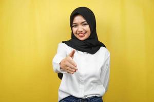 mooie jonge aziatische moslimvrouw die vol vertrouwen glimlacht, met handen die de camera schudden, handenteken van samenwerking, handteken van overeenkomst, handteken van vriendschap, geïsoleerd op gele achtergrond