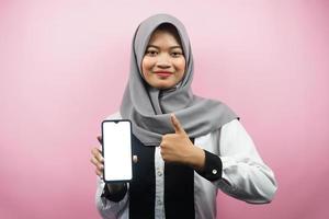 mooie jonge Aziatische moslimvrouw glimlachend vol vertrouwen en opgewonden met handen met smartphone, presentatie van toepassing, ok teken hand, goed gedaan, succes, geïsoleerd op roze achtergrond foto