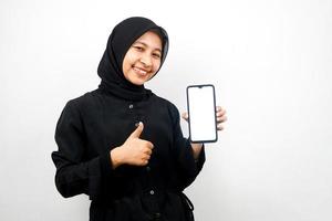 mooie jonge aziatische moslimvrouw met handen die smartphone vasthouden, toepassing promoten, zelfverzekerd en opgewonden glimlachen, ok teken hand, goed gedaan, succes, geïsoleerd op witte achtergrond foto