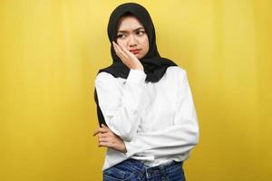 Mooie Aziatische jonge moslimvrouw denken, op zoek naar ideeën, op zoek naar oplossingen voor problemen, met handen met wangen, geïsoleerd op gele achtergrond foto