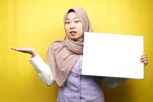 mooie jonge moslimvrouw verwarren, hand met lege lege banner, plakkaat, wit bord, leeg bord, wit reclamebord, iets presenteren in kopieerruimte, promotie