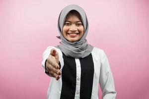 mooie jonge Aziatische moslimvrouw glimlachend vol vertrouwen, met handen schudden van de camera, handen teken van samenwerking, hand teken van overeenkomst, hand teken van vriendschap, geïsoleerd op roze achtergrond foto