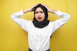 mooie jonge Aziatische moslimvrouw geschokt, verrast, wow uitdrukking, handen met hoofd, geïsoleerd op gele achtergrond foto
