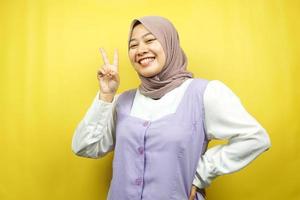 mooie jonge Aziatische moslimvrouw steenbolk met v-ondertekende handen, ok, goed gedaan, overeenkomst, overwinning, kijkend naar camera geïsoleerd op gele achtergrond foto