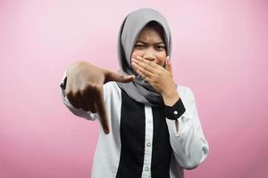 Mooie jonge moslimvrouw met hand die mond bedekt, hand naar beneden wijst, afkeuringsuitdrukking toont, walging toont van iets, geïsoleerd op roze achtergrond foto