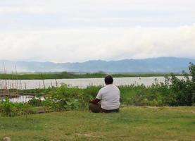 een dikke man zit ontspannen aan de rand van het limboto-meer, gorontalo foto
