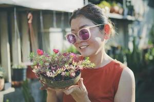 mooie vrouw die pot met bloeiende bloem opvoedt met een geluksgezicht foto