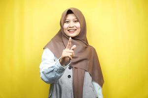 Mooie jonge Aziatische moslimvrouw glimlachend zelfverzekerd en vrolijk, met handen wijzend op camera, wijzend op publiek, wijzend naar klant, geïsoleerd op gele achtergrond
