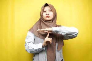 Mooie Aziatische jonge moslimvrouw met hand met stopbord, stille tekenhand, spreek geen tekenhand, maak geen lawaaitekenhand, geïsoleerd op gele achtergrond