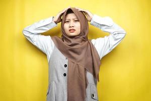mooie jonge Aziatische moslimvrouw geschokt, verrast, wow uitdrukking, handen met hoofd, geïsoleerd op gele achtergrond foto