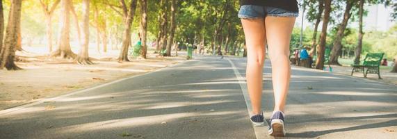 Aziatische vrouw benen tijdens het joggen in het park bedekt met veel bomen en warm zonlicht. jonge vrouw benen close-up tijdens het hardlopen in het park. buitenactiviteit in het parkconcept. panoramische banner. foto