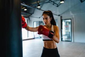 jonge azië dame kickboksen oefening training bokszak stoere vrouwelijke vechter praktijk boksen in gym fitness klasse. sportvrouw recreatieve activiteit, functionele training, gezonde levensstijl concept. foto