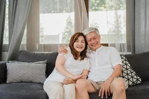 Aziatische senior paar ontspannen thuis. Aziatische senior chinese grootouders, man en vrouw gelukkige glimlach knuffel samen praten terwijl liggend op de bank in de woonkamer thuis concept. foto