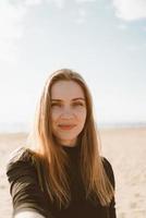 portret van mooie vrouw met lang haar, blonde neemt selfie op mobiele telefoon op zandstrand foto