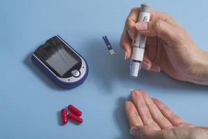 vrouw meet bloedsuikerspiegel met een glucometer.diabetes concept op blauwe achtergrond foto