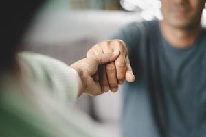 vrouwelijke vriend of familie zitten en houden elkaars hand vast tijdens het opvrolijken van de mentaal depressieve man, psycholoog biedt mentale hulp aan de patiënt. ptss geestelijke gezondheidsconcept foto