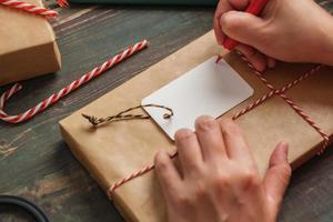 vrouw schrijft cadeau-tag en bevestig aan kerstcadeau op houten tafel foto