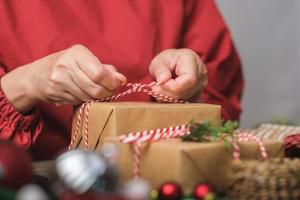 vrouw die kerst handgemaakte geschenkdoos maakt met bruin papier kromtrekken met kerst decor op houten tafel foto