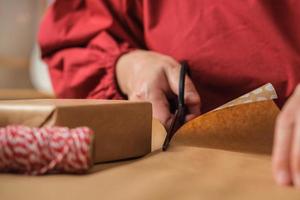 close-up vrouw hand snijden kraftpapier om kerstcadeaudoos op houten tafel te verpakken foto