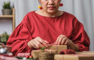 vrouw die kerst handgemaakte geschenkdoos maakt met bruin papier kromtrekken met kerst decor op houten tafel foto