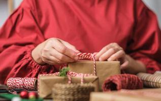 vrouw die kerst handgemaakte geschenkdoos maakt met bruin papier kromtrekken met kerst decor op houten tafel foto