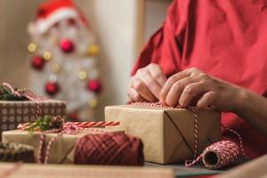 vrouw die kerst handgemaakte geschenkdoos maakt met bruin papier kromtrekken met kerst decor op houten tafel foto