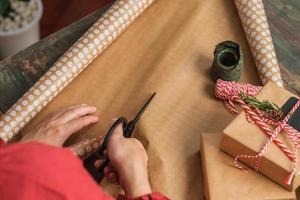 close-up vrouw hand snijden kraftpapier om kerstcadeaudoos op houten tafel te verpakken foto