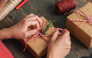 vrouw die kerst handgemaakte geschenkdoos maakt met bruin papier kromtrekken met kerst decor op houten tafel foto