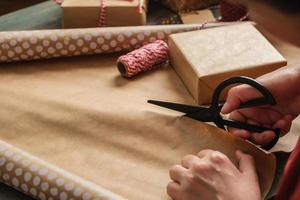close-up vrouw hand snijden kraftpapier om kerstcadeaudoos op houten tafel te verpakken foto