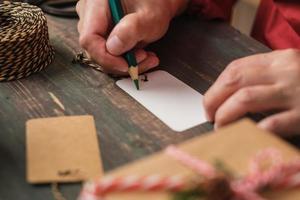 vrouw schrijft cadeau-tag en bevestig aan kerstcadeau op houten tafel foto