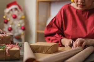 close-up vrouw hand snijden kraftpapier om kerstcadeaudoos op houten tafel te verpakken foto