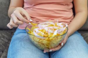 een bord chips en een centimeter tape in de handen van het meisje. junk food. het concept van de strijd tegen overgewicht. selectieve aandacht, filmkorrel. foto